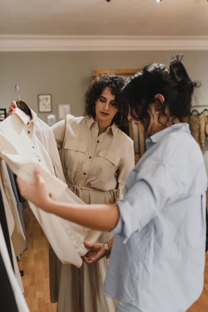 Offerings Two women shopping and discussing clothes in a stylish boutique, focusing on a beige shirt.