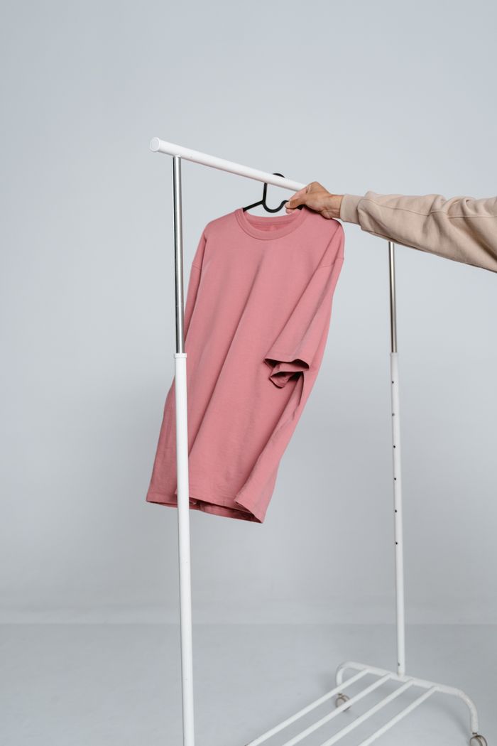 Offerings Pink shirt hanging on a white clothing rack in a minimalist setting.