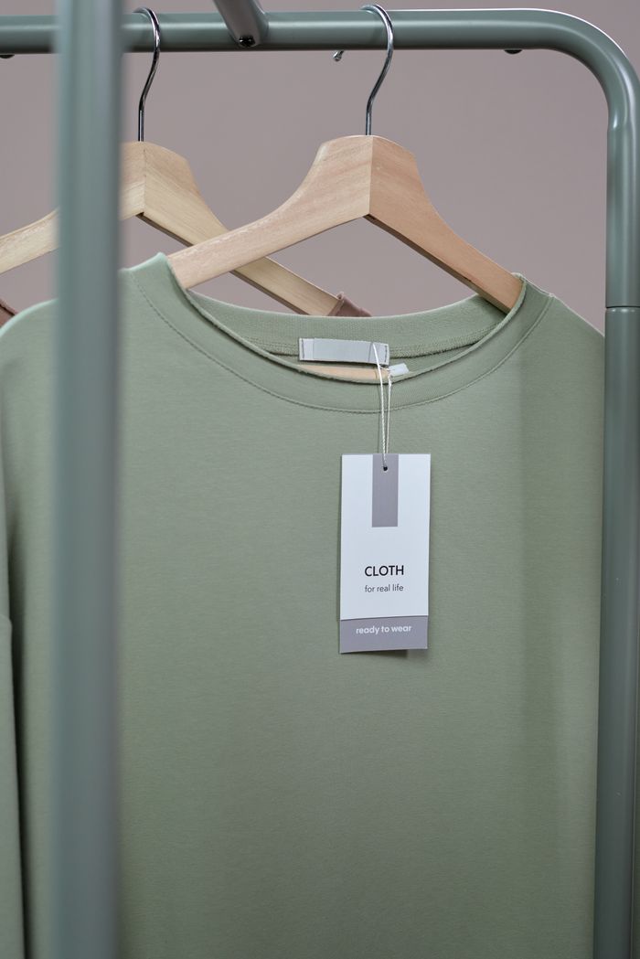 The Art of Drawing Readers In: Your attractive post title goes here A simple green t-shirt with a tag hanging on a wooden hanger against a neutral background.